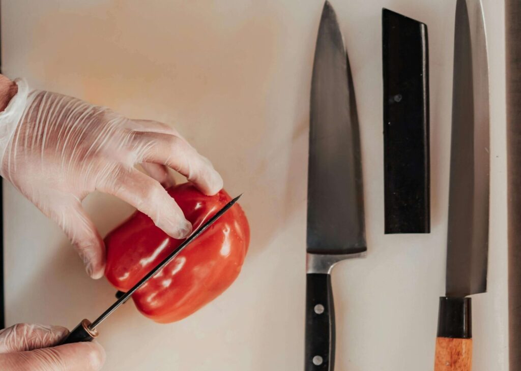 Chef cutting a bred bell peper with three chef knives next to him.