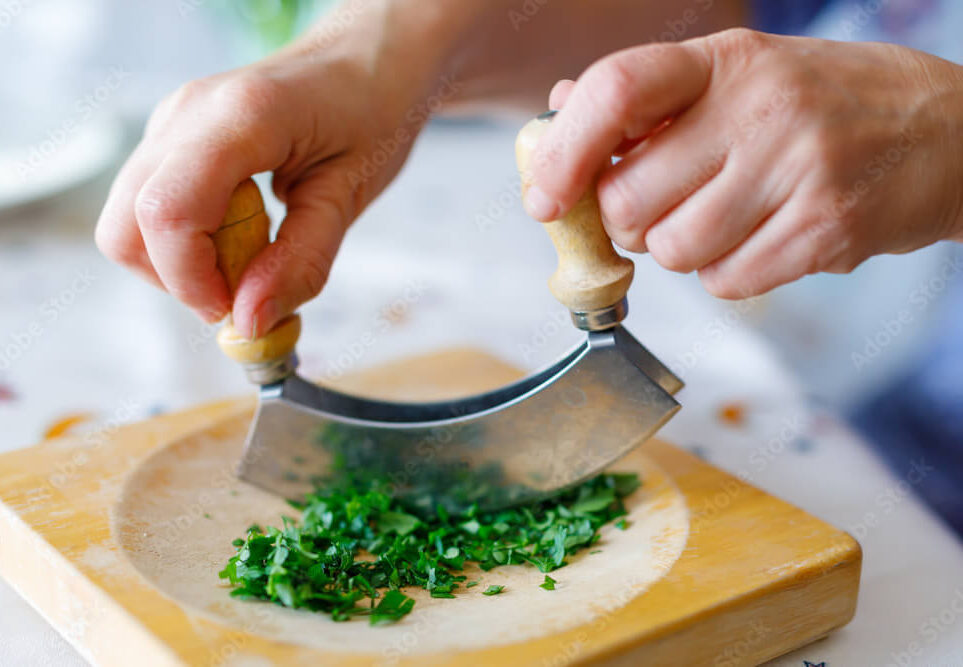 Chef using a small mezzaluna knife to mince herbs