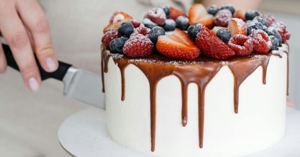 Woman cutting a white cake covered with chocolate and fruits