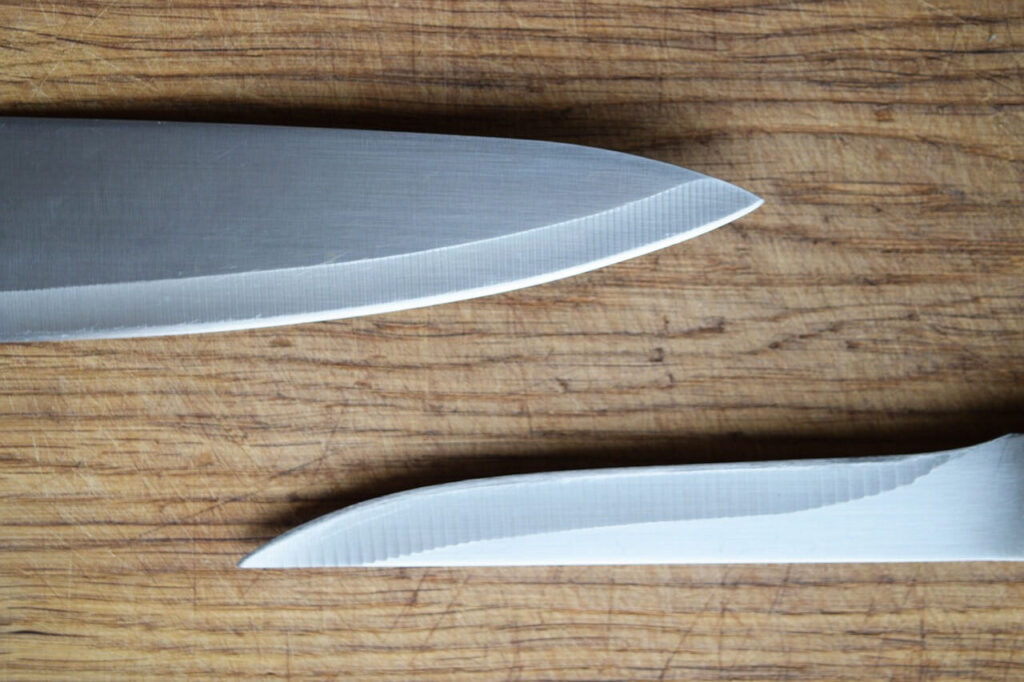 5 The tips of two stainless steel knives from a side view. A chef knife and a fillet knife.
