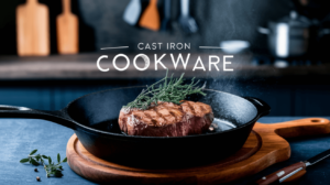 a pan of seared steak with a sizzling effect. The steak is cooked to medium-rare and is placed in a cast iron skillet. The skillet is placed on a wooden board with a few fresh herbs scattered around it. The background is blurred, showing a rustic kitchen with wooden elements and a few cooking utensils.
